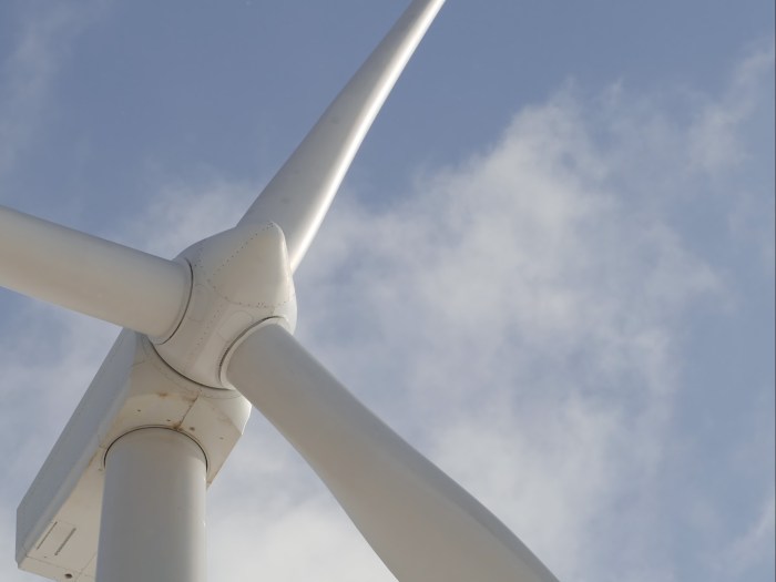 Up close view of a wind turbine with light blue sky and clouds in background