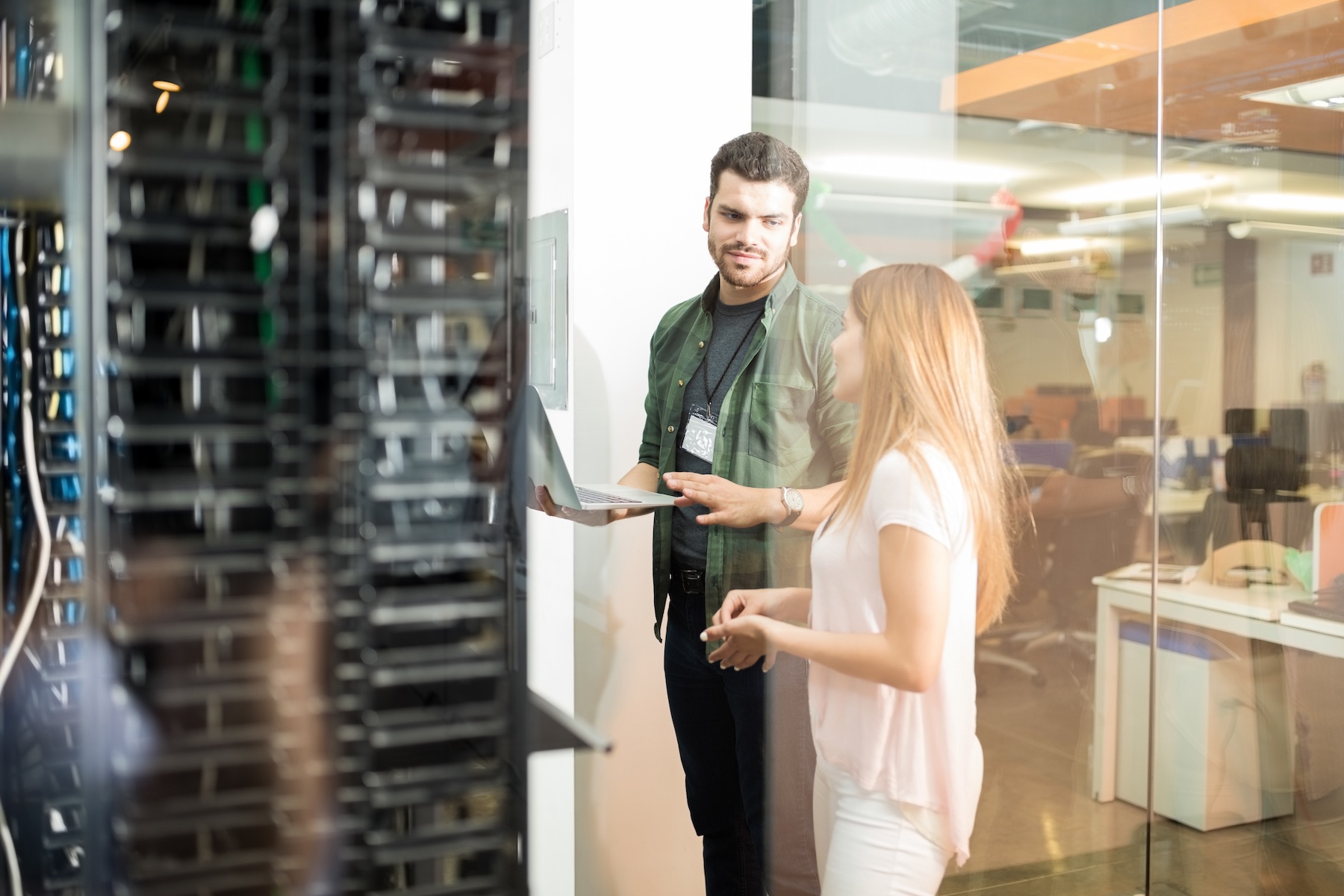 Two business people standing in server room with laptop and discussing.