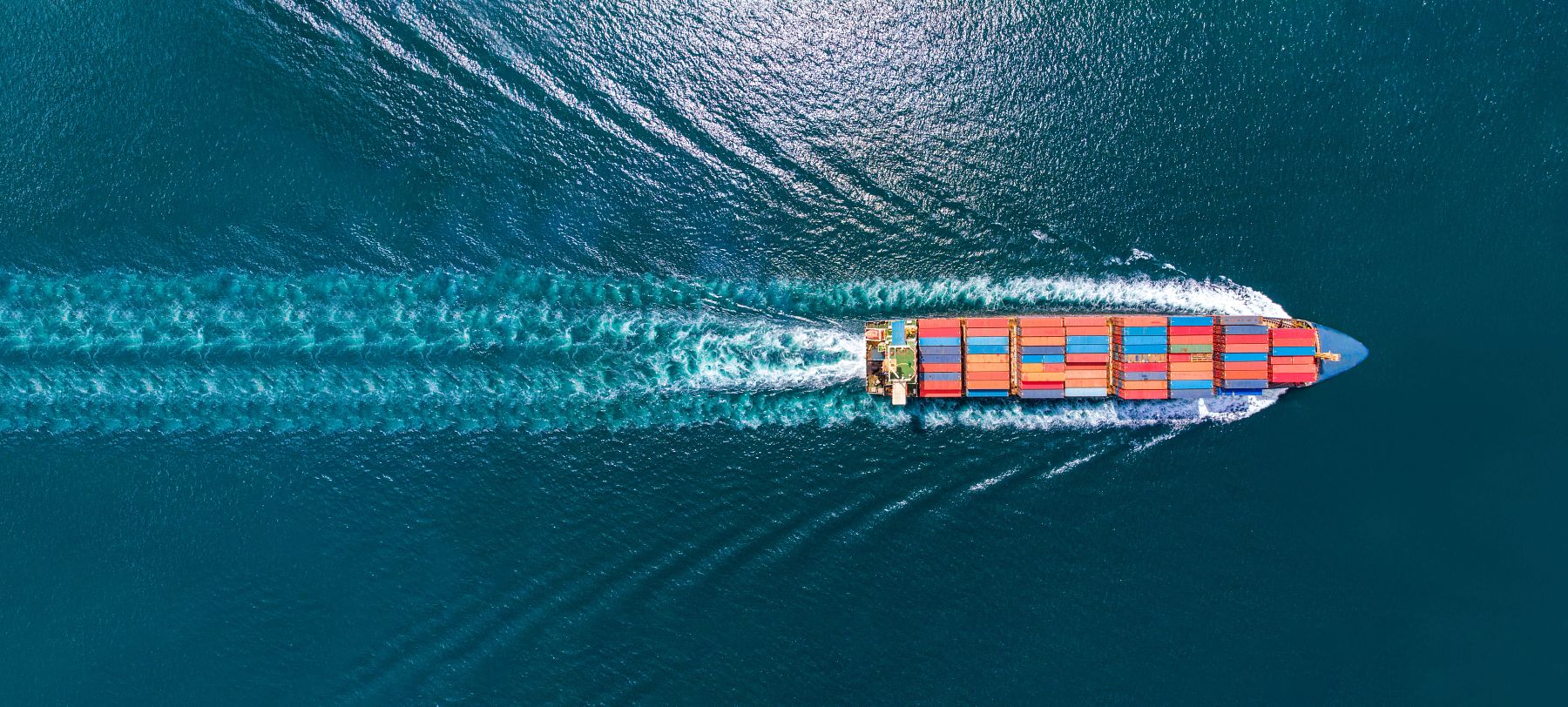 Aerial top view of cargo ship with contrail in the ocean