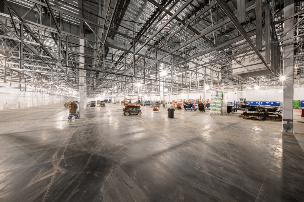 Interior view of a warehouse floor with some construction materials visible in background.