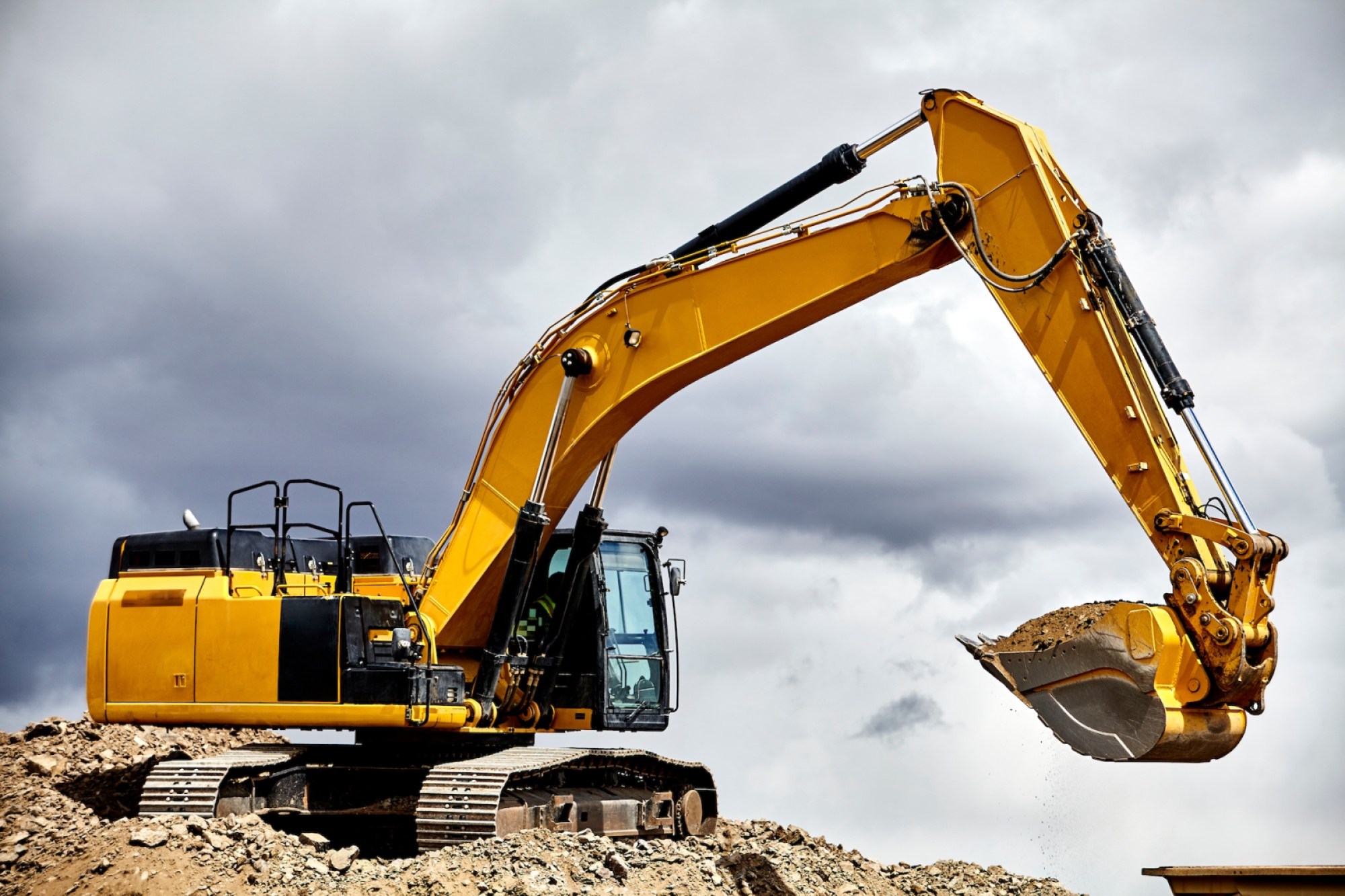 Construction industry heavy equipment excavator moving gravel at jobsite quarry with stormy skies