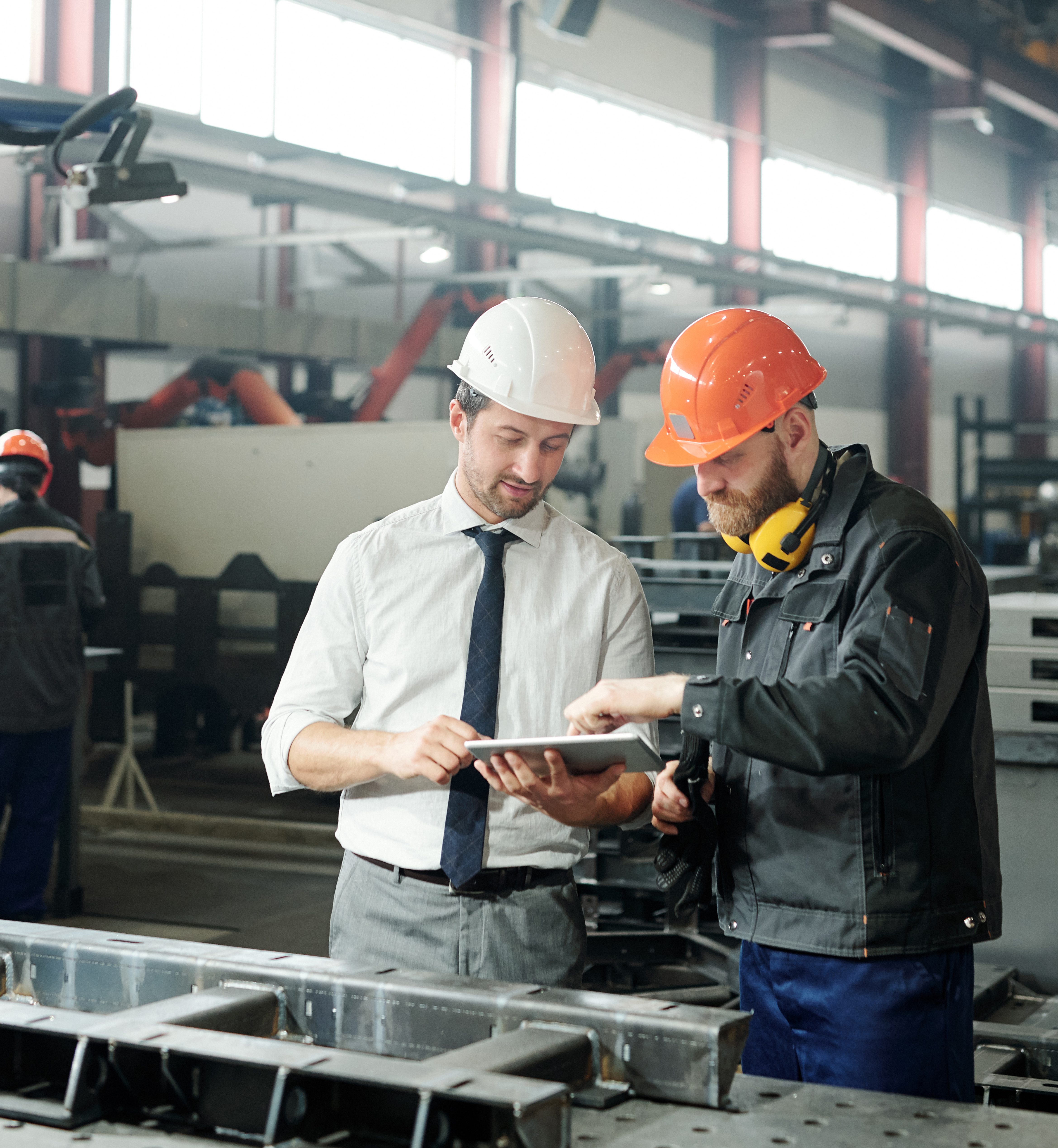 Technician in formalwear using tablet while engineering industrial machine with factory worker in workshop