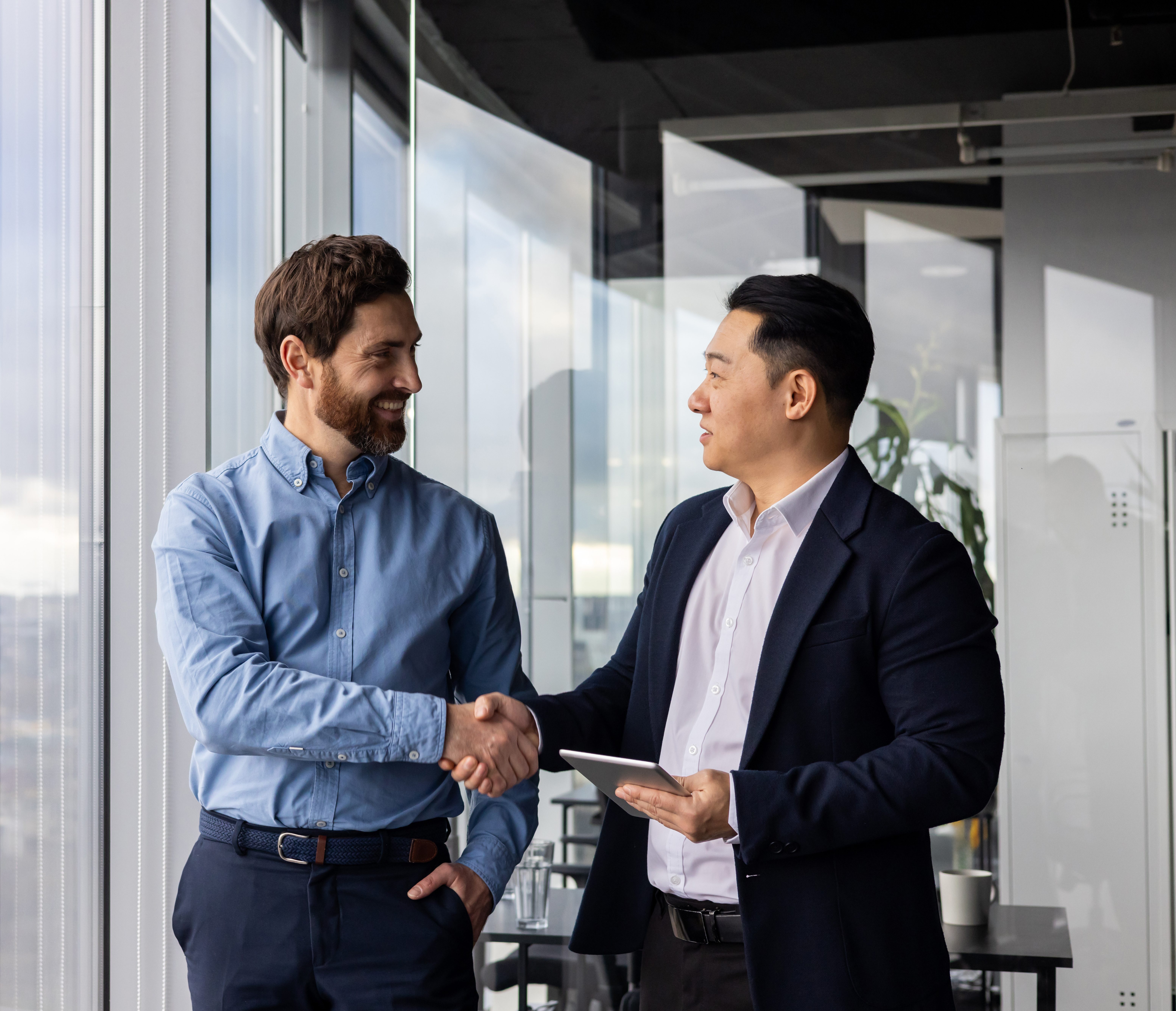 Two professional businessmen shaking hands in a modern office, symbolizing partnership, collaboration, and successful business agreement.